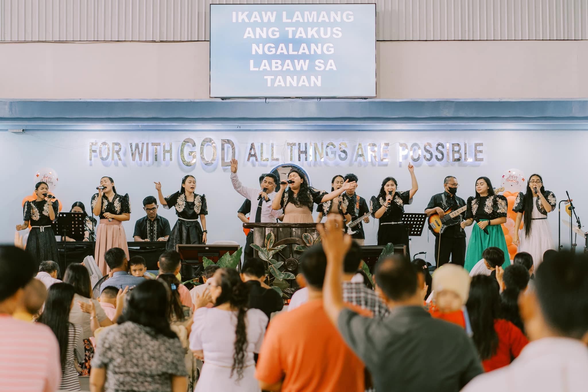 The worship team leading the congregation in song beneath the words "For with God all things are possible"