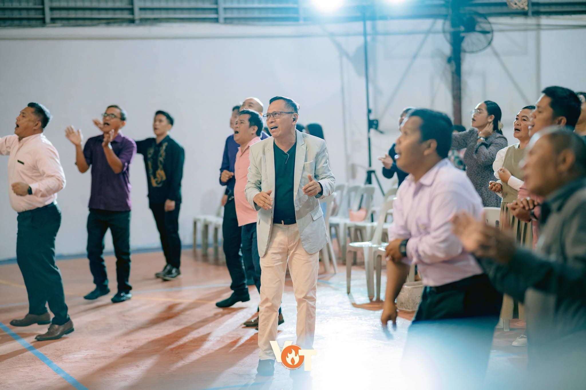 A large, diverse crowd of worshipers with hands raised during a service