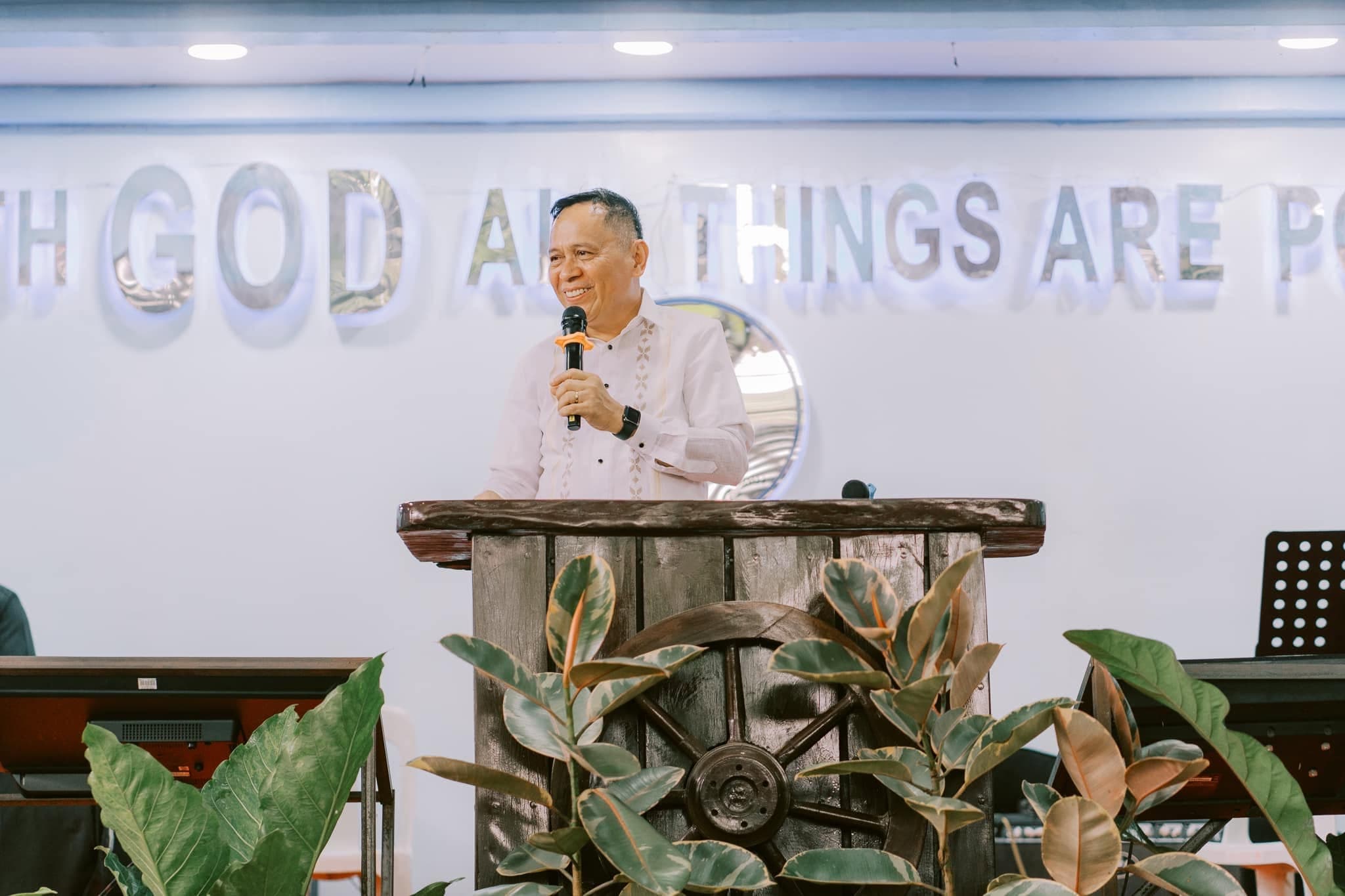 Rev. Mario Magno preaching at the UPC VOT Mintal pulpit, with “For with God all things are possible” on the wall behind him